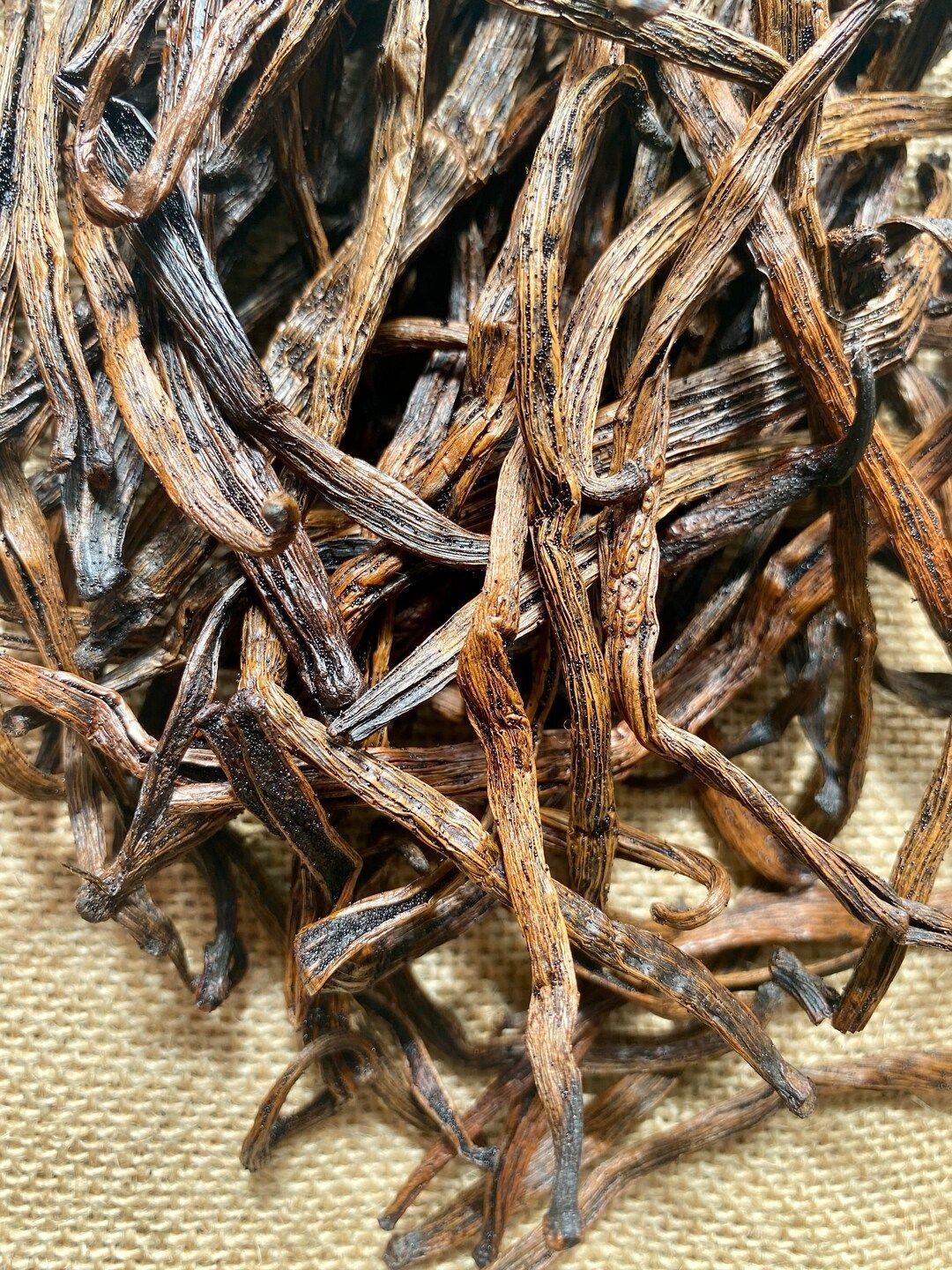 Close-up of dried vanilla beans in a tangled pile over a burlap surface.